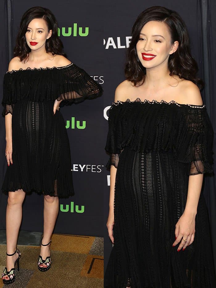 Christian Serratos embraces effortless maternity elegance in a black off-the-shoulder lace dress, pairing it with floral-embroidered platform sandals and bold red lips for a striking finish