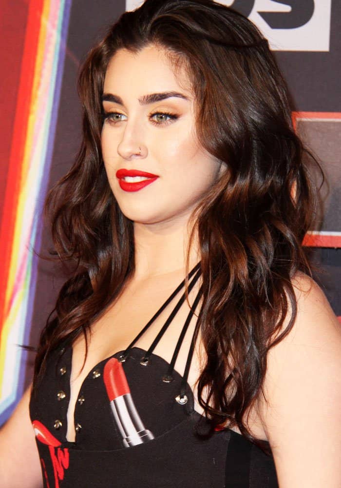 Lauren Jauregui stuns with voluminous waves and a bold red lip, perfectly complementing her edgy black dress adorned with a striking lipstick graphic
