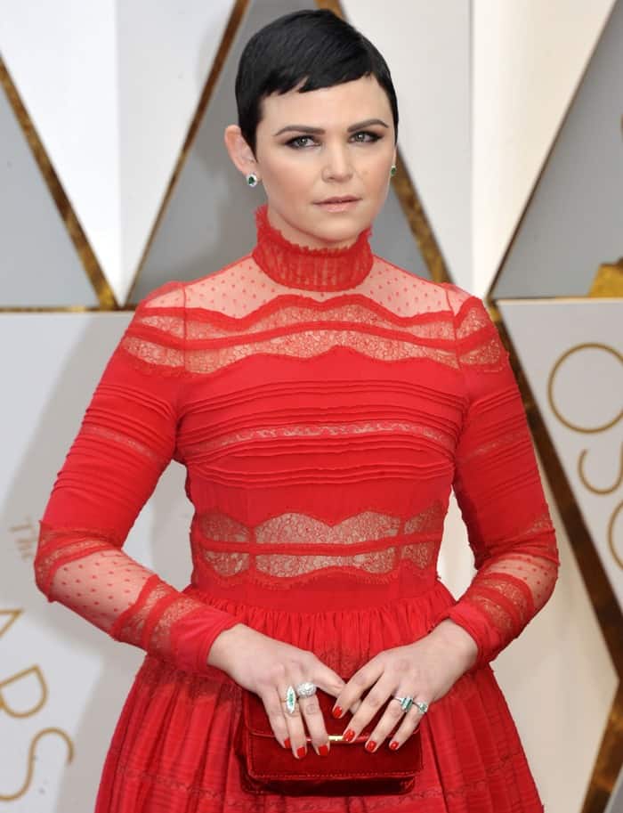 Ginnifer Goodwin accessorized her red lace gown with emerald green stud earrings, silver statement rings, and a red clutch, adding subtle pops of contrast to her monochromatic look