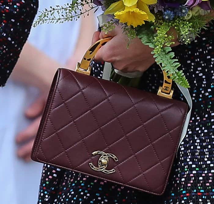 Kate Middleton carried a burgundy Chanel calfskin flap bag with a distinctive gold enamel handle, perfectly complementing her elegant floral bouquet