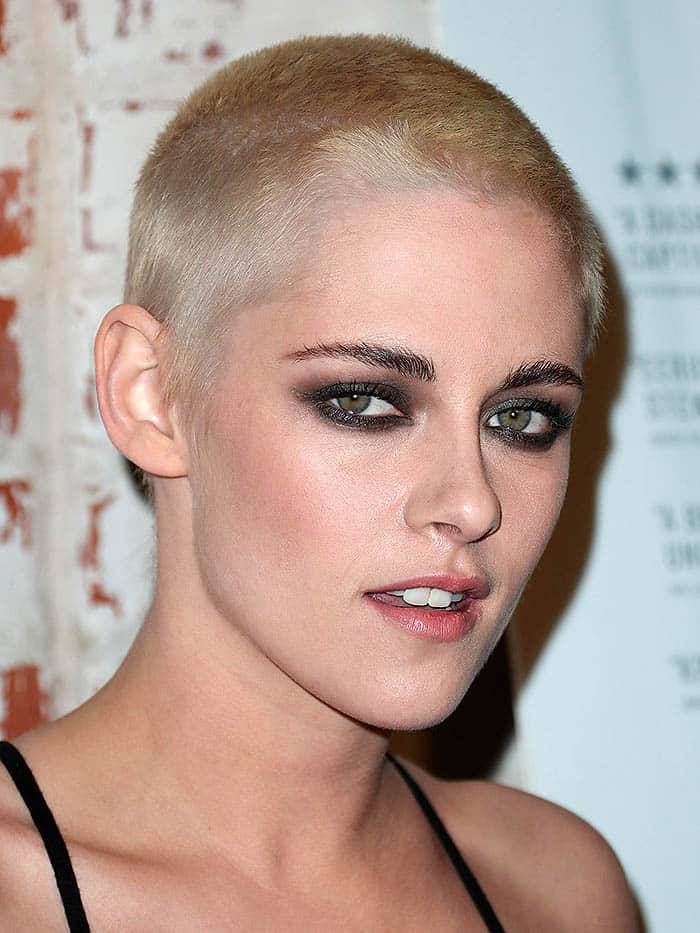 Kristen Stewart showcases her edgy blonde buzz cut with smoky eye makeup, emphasizing her striking green eyes and confident style
