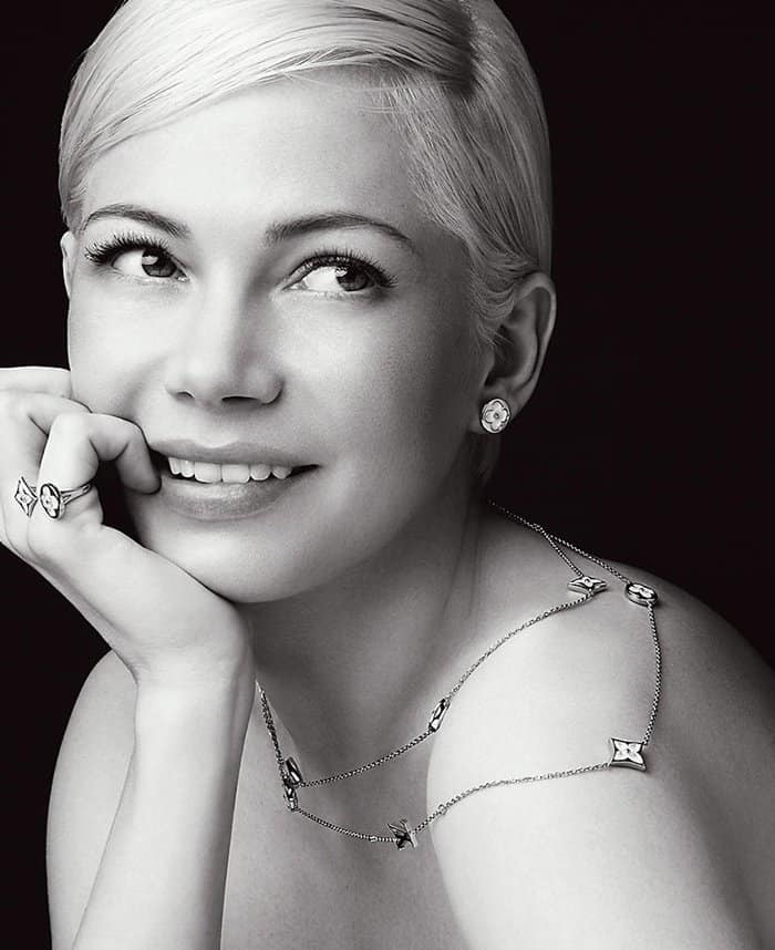 Michelle Williams stuns in a timeless black-and-white portrait, showcasing Louis Vuitton’s BB Blossom collection with diamond-studded floral earrings, a delicate chain necklace, and matching statement rings