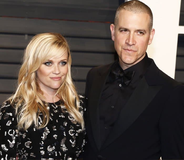 Reese Witherspoon radiates elegance in a sequined black dress while posing alongside her husband, Jim Toth, at the star-studded Vanity Fair Oscars Party