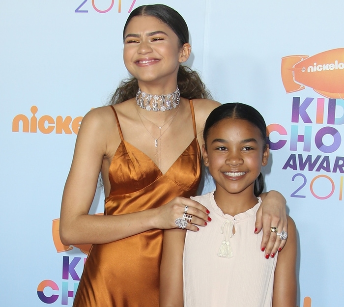 Zendaya shines in a burnt orange satin slip dress paired with a dazzling bejeweled choker, while her young niece looks adorable in a soft pastel dress with delicate bow details