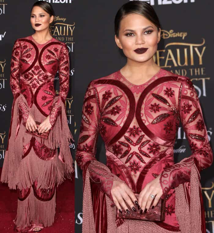 Chrissy Teigen wearing a dark red embellished gown from Raisa & Vanessa at the 'Beauty and the Beast' Hollywood premiere