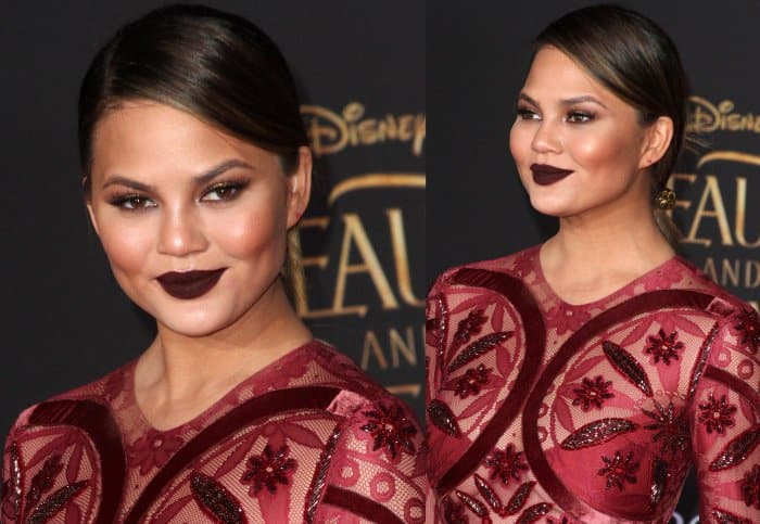 Chrissy Teigen wearing a dark red embellished gown from Raisa & Vanessa at the 'Beauty and the Beast' Hollywood premiere