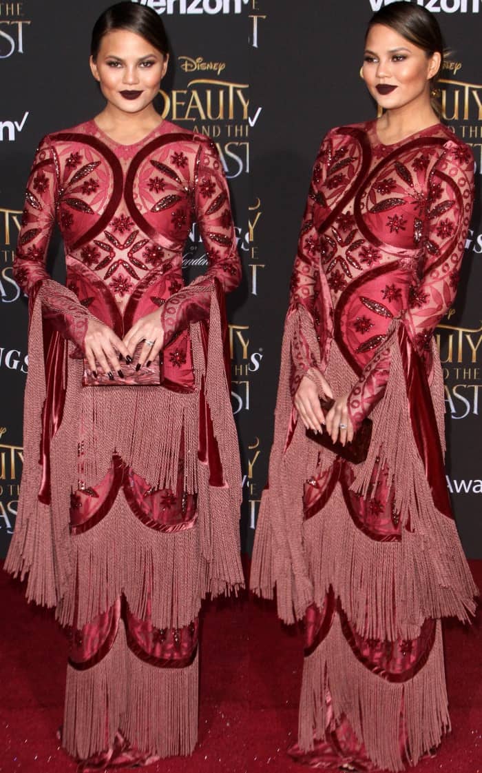 Chrissy Teigen wearing a dark red embellished gown from Raisa & Vanessa at the 'Beauty and the Beast' Hollywood premiere