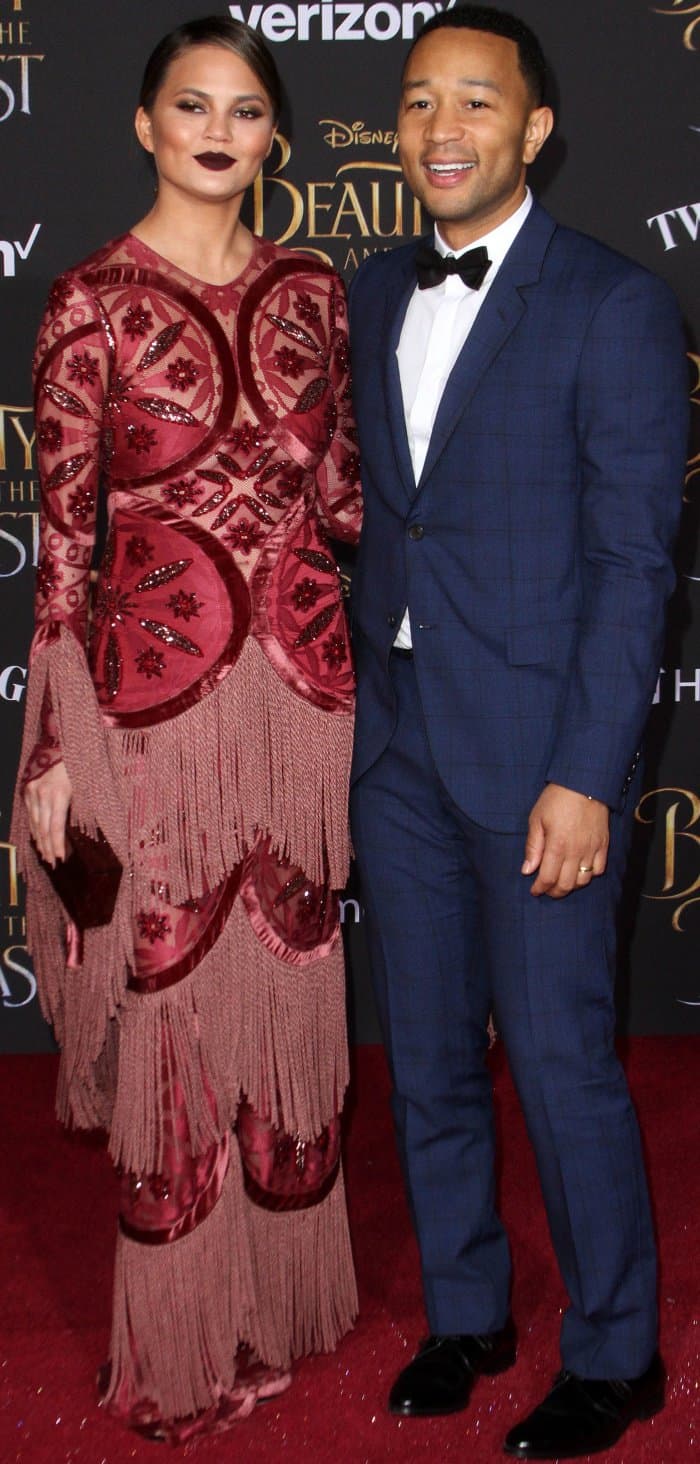 Chrissy Teigen stuns in a bold Raisa & Vanessa gown with intricate embellishments and fringe, while John Legend complements her in a sleek navy tuxedo with a black bow tie