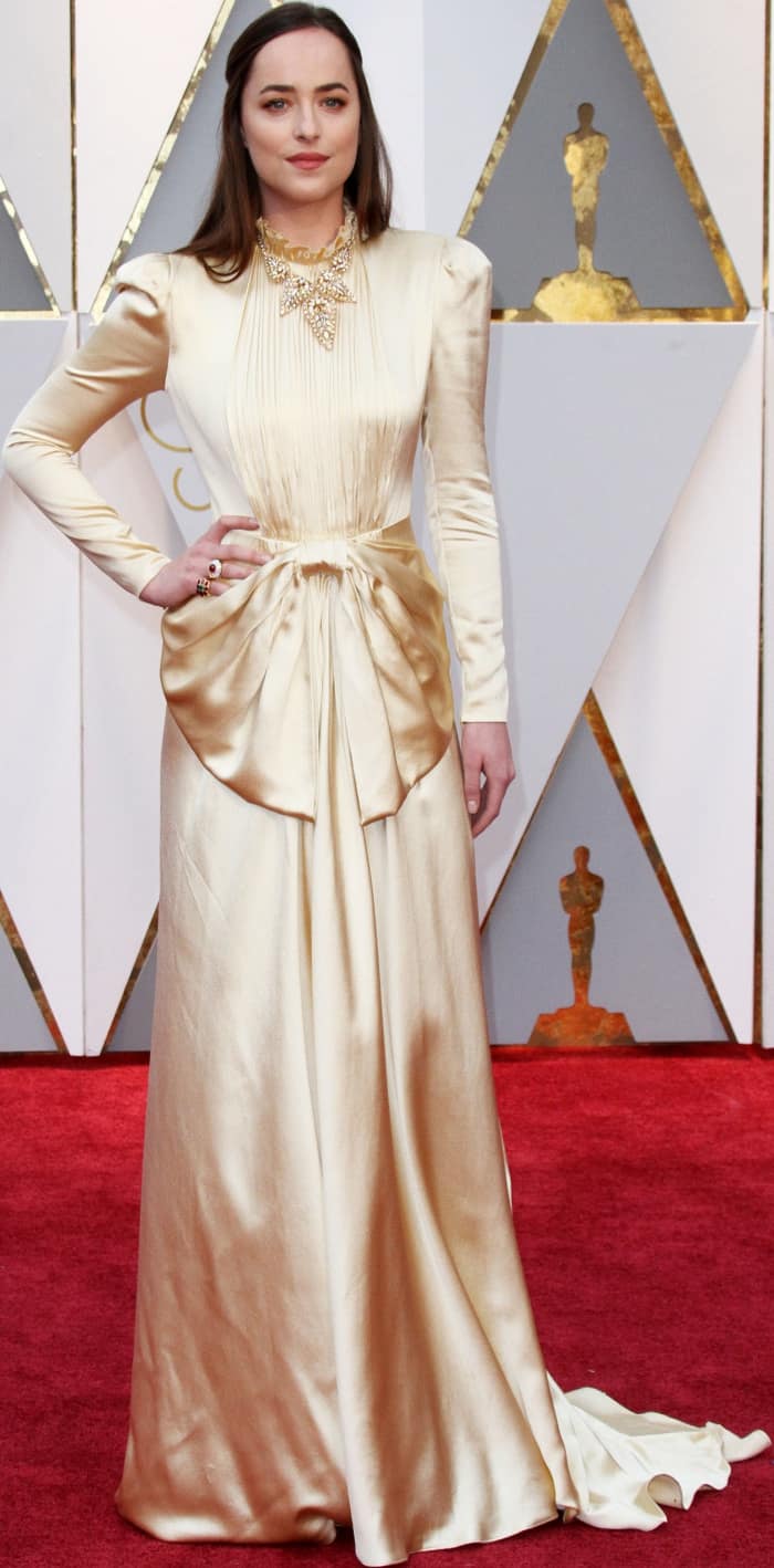 Dakota Johnson dazzled in a vintage-inspired gold Gucci gown featuring a ruffled collar, a bow-accented waist, and a flowing train at the 89th Academy Awards