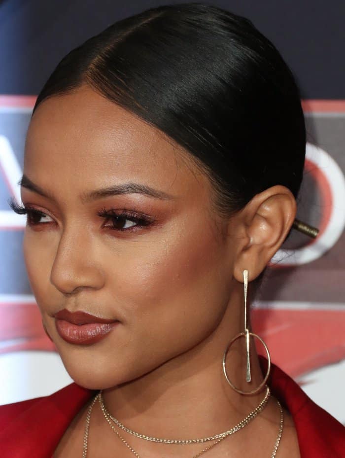Karrueche Tran's makeup featured a warm, bronzed glow with shimmery burgundy eyeshadow, fluttery lashes, and a glossy nude lip, perfectly complementing her bold red ensemble