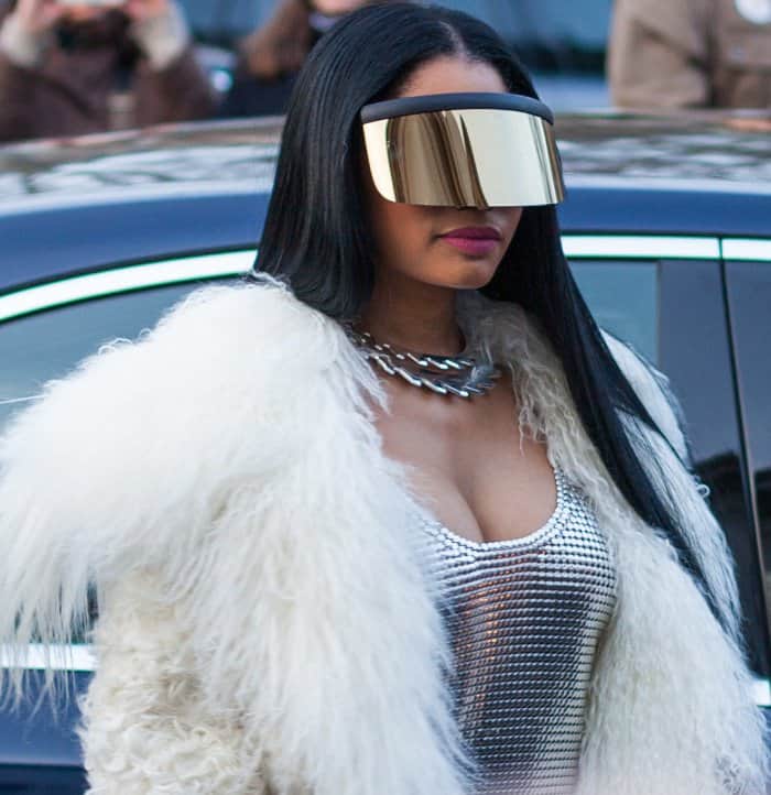 Nicki Minaj exudes futuristic glamour in a metallic chainmail dress, oversized mirrored visor, and a luxe white fur coat