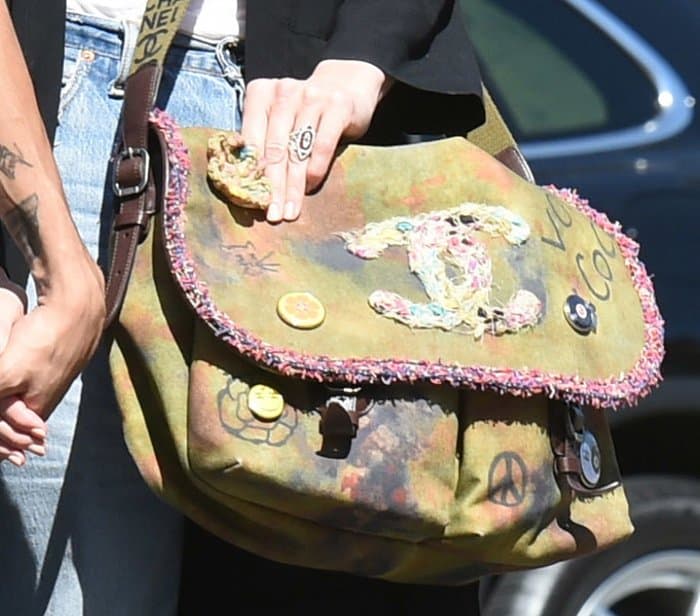 In this close-up, Ashlee Simpson showcases her edgy Chanel Graffiti Messenger Bag, detailed with colorful patches, peace signs, and hand-drawn designs, while wearing a statement silver ring with an intricate oval-shaped motif