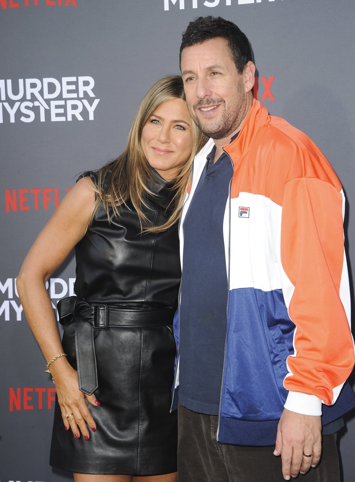 Jennifer Aniston stuns in a belted black leather mini dress, while Adam Sandler keeps it casual in a retro Fila jacket at the Netflix premiere of Murder Mystery at Village Theatre Westwood on June 10, 2019