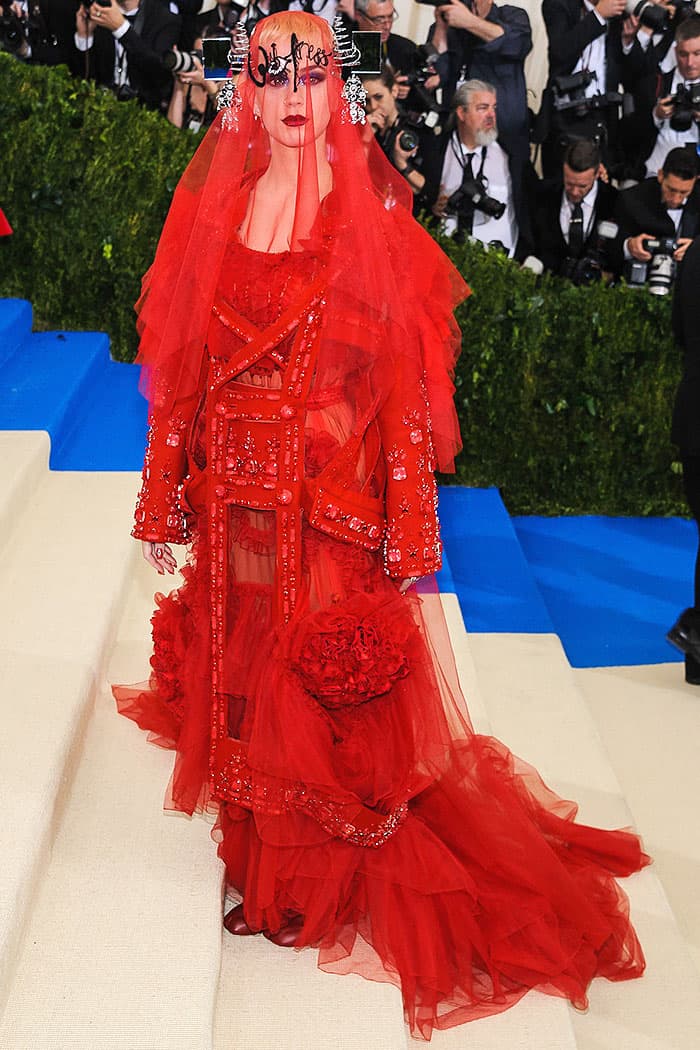 Arriving in style, Katy Perry embraces the Met Gala's celebration of avant-garde fashion with her elaborate Maison Margiela Couture gown, detailed nail art, and statement Lorraine Schwartz jewelry