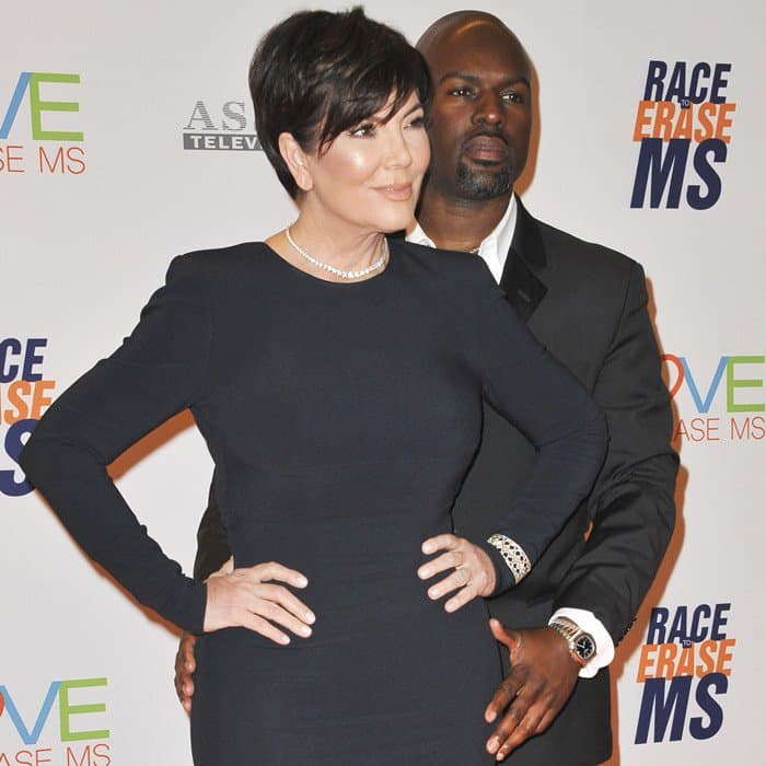 Kris Jenner accessorized with a wide metal bracelet over the sleeve on her left arm, a glittering diamond necklace, and stud earrings