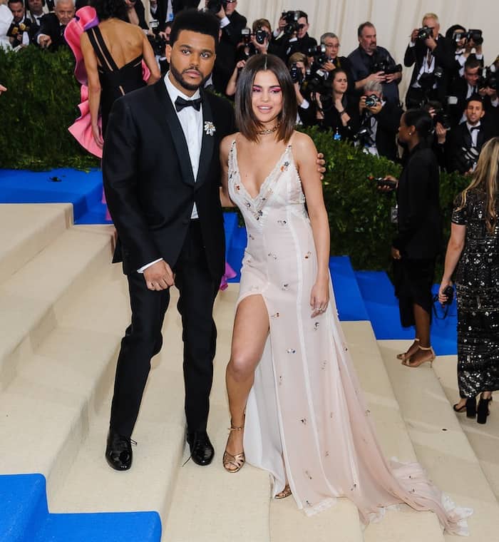 Selena Gomez stuns in a custom Coach slip dress with thigh-high slit and metallic ankle-strap sandals, while The Weeknd keeps it classic in a black tuxedo at the 2017 MET Gala