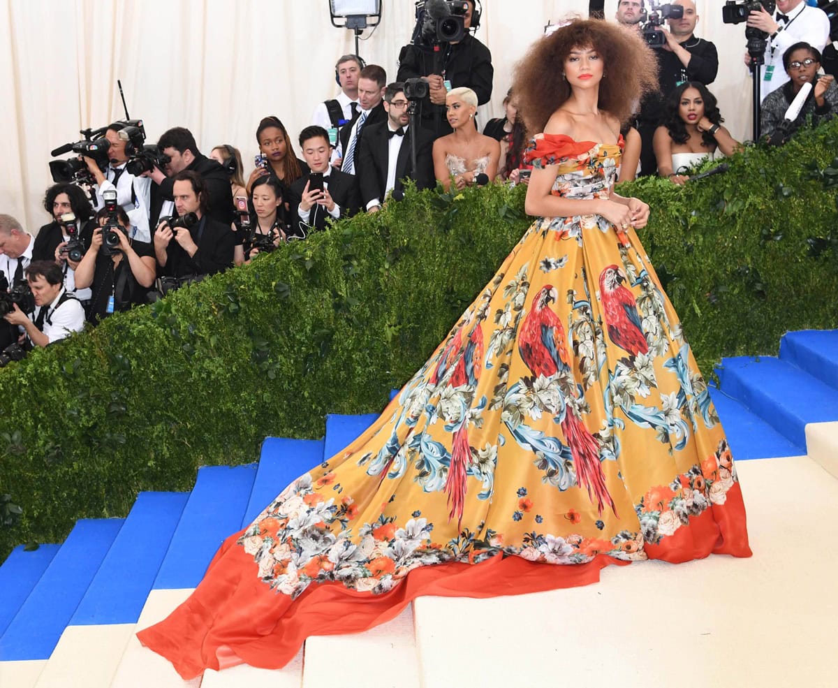 Zendaya stuns at the 2017 Met Gala in a vibrant off-the-shoulder Dolce & Gabbana Alta Moda gown adorned with tropical parrots and a sweeping orange-lined train