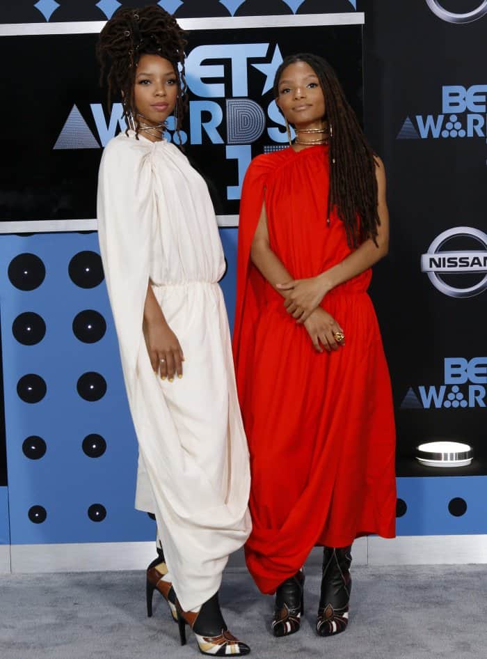 Chloe and Halle Bailey stun at the BET Awards in coordinated draped Ms MIN dresses—Chloe in ivory and Halle in vibrant red—paired with bold Rodarte heels