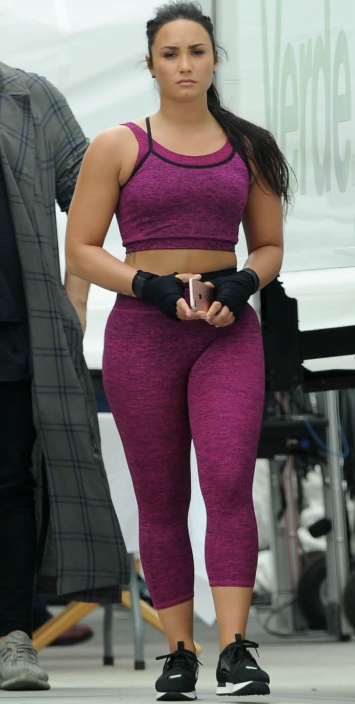 Demi Lovato wearing purple Fabletics workout gear and black sneakers on the set of the new Fabletics commercial shoot