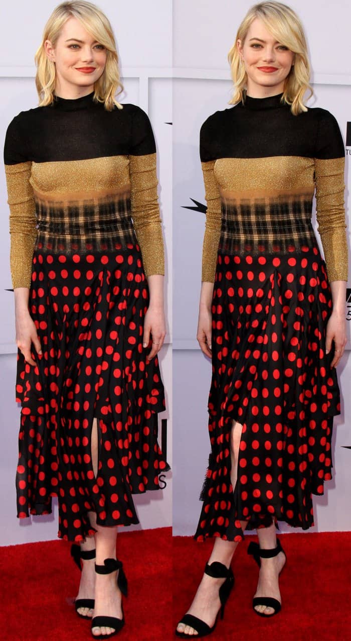Emma Stone masterfully balances bold patterns by pairing a gold and plaid top with a red polka-dot skirt, finishing the look with minimalist black ankle-strap heels to keep the focus on her statement ensemble