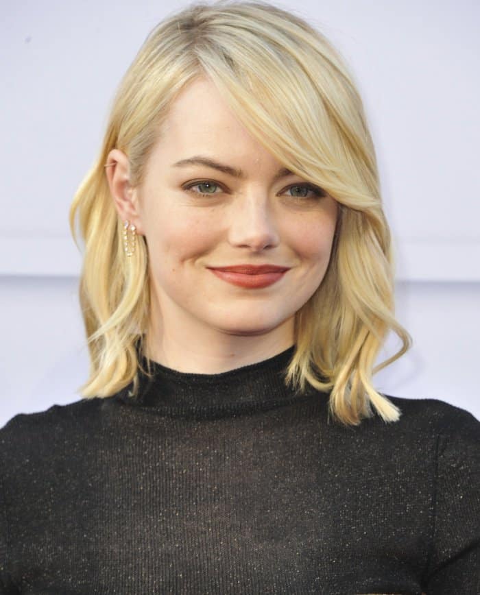 Emma Stone’s makeup features a flawless base, soft blush, and a warm terracotta lip that highlights her radiant complexion, while her delicate gold ear cuffs add a subtle touch of modern elegance to her look