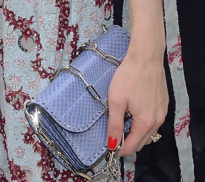 Olivia Palermo’s lavender Valentino Rockstud clutch features textured leather, silver chain detailing, and signature stud embellishments for a polished yet edgy finish