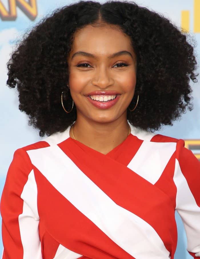 Yara Shahidi beams with a natural glow, showcasing her voluminous curls and chic hoop earrings