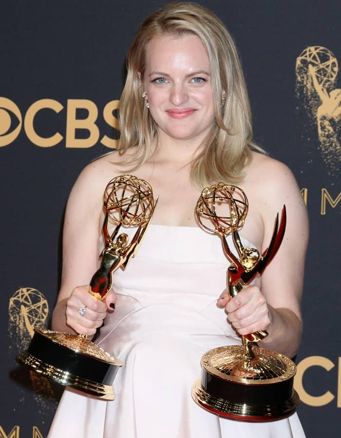 Elisabeth Moss poses with two Emmy trophies on the red carpet.