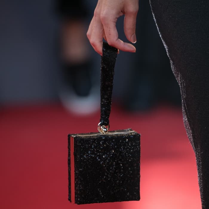 Rebecca Hall adds a touch of glamour with a black glittery box clutch featuring a structured design and a sleek wrist strap