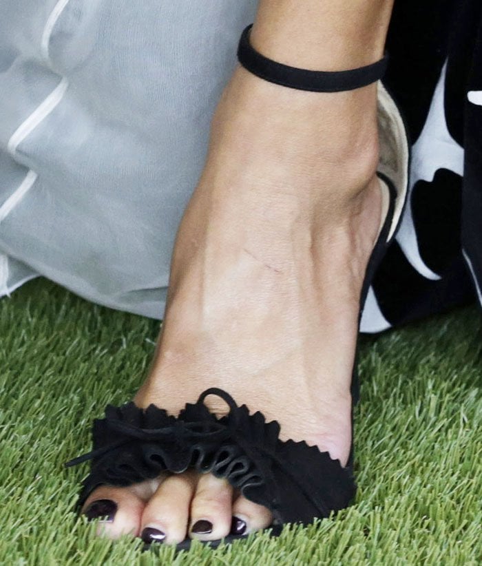 Nicole Scherzinger flaunts a dark, glossy pedicure in ruffled black Alexander White "Eva" sandals that perfectly balance elegance and edge