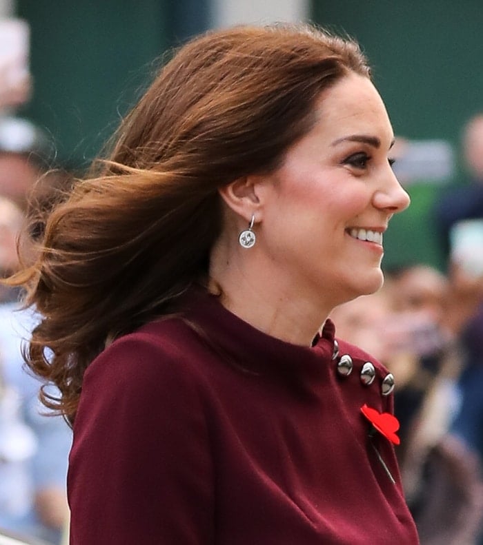 Kate Middleton radiates elegance, accessorizing her wine-colored tunic dress with Mappin & Webb 'Empress' diamond drop earrings and a striking red Remembrance poppy pin
