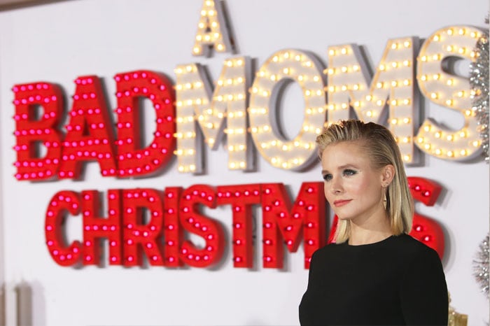 Kristen poses beside the promos signage for "A Bad Moms Christmas"