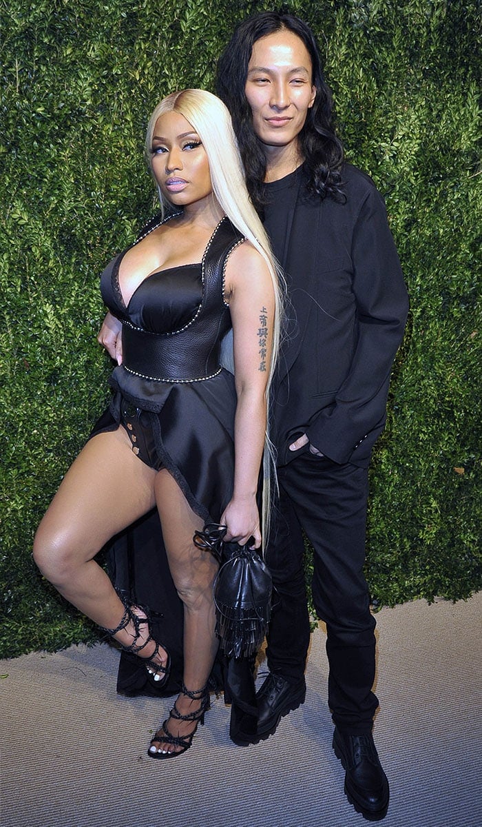 Nicki Minaj posing with designer Alexander Wang in her custom Alexander Wang lace-trimmed silk gown, ball-studded leather harness, snap-front leather shorts, fringed leather bag, and barbed leather lace-up sandals.