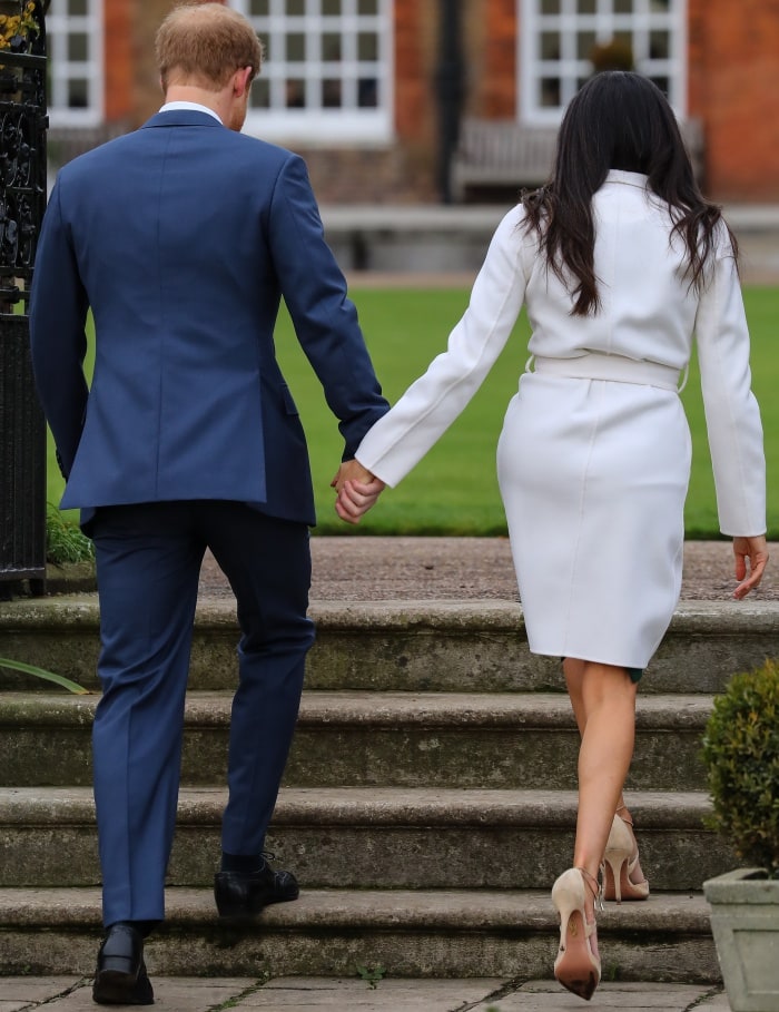 Prince Harry wearing a classic navy suit and Meghan Markle wearing a Line coat, P.A.R.O.S.H. dress, and Aquazzura heels