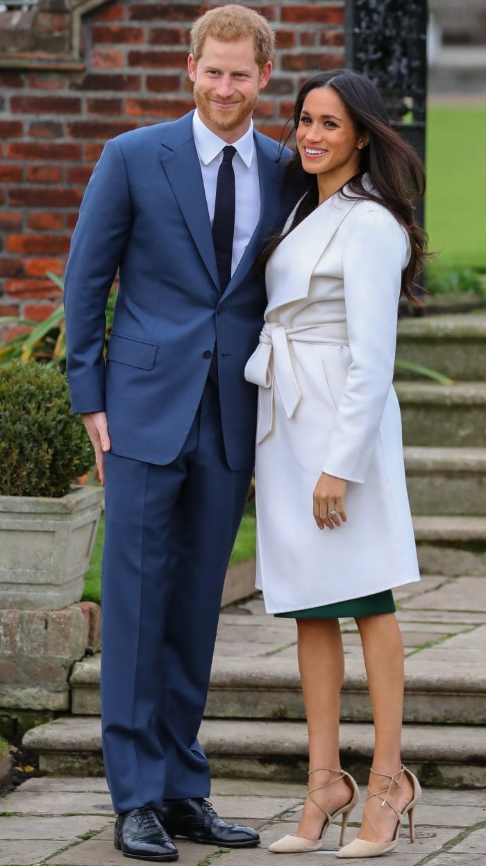 Prince Harry wearing a classic navy suit and Meghan Markle wearing a Line coat, P.A.R.O.S.H. dress, and Aquazzura heels