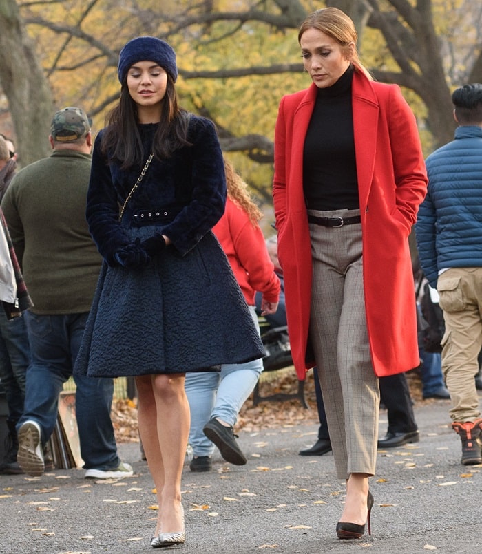 Jennifer Lopez stuns in a bold red coat layered over a black turtleneck, checked trousers, and classic black pumps, while Vanessa Hudgens looks chic in a navy velvet coat dress with pointy-toe heels as they film Second Act in New York City on December 4, 2017