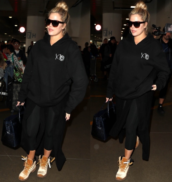Khloé Kardashian wearing a black hoodie, cropped black leggings, and Timberland x Off-White leather lace-up boots at the Los Angeles International Airport