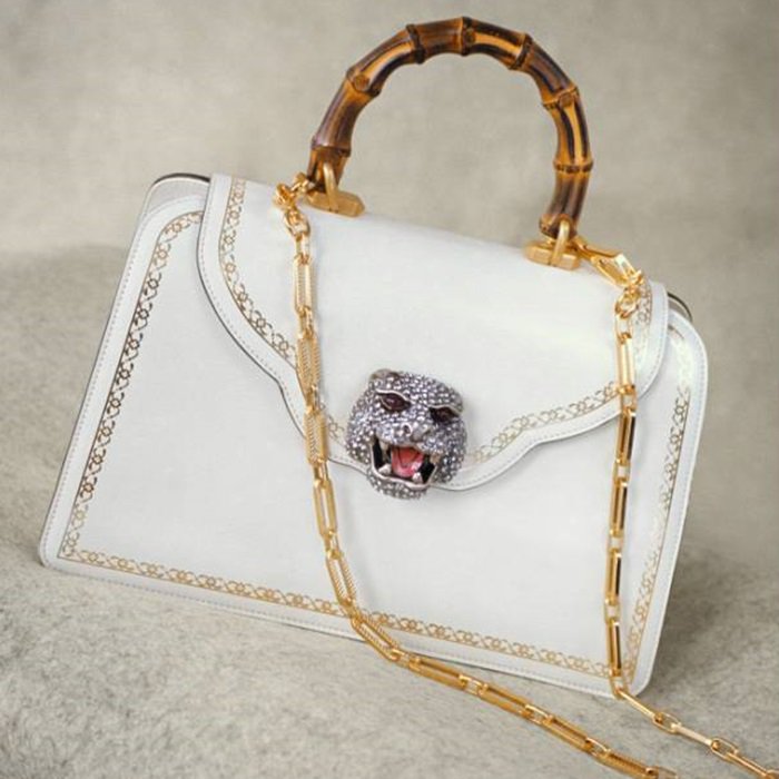 A crystal-studded cat head adds feline flair to the scalloped flap of an exquisite leather bag, stamped with gilt accents and topped with a curvy bamboo handle