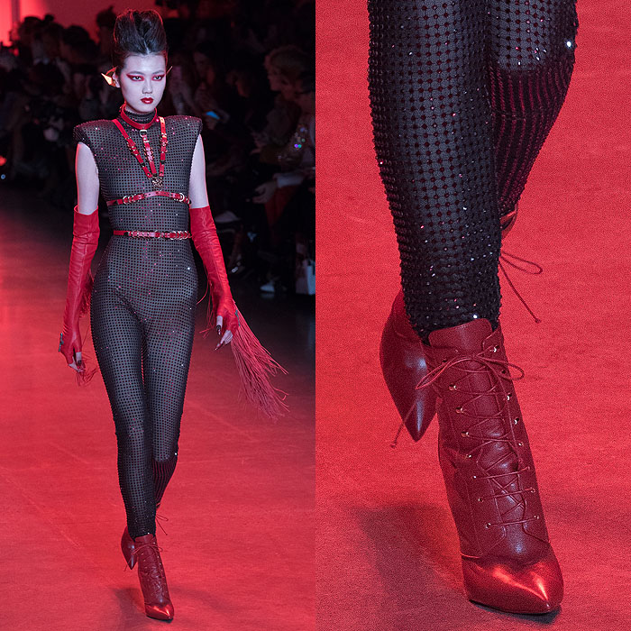 A model wearing a crystal-mesh bodysuit with a red leather harness, fringed fingerless gloves, and Christian Louboutin for The Blonds red leather lace-up booties.