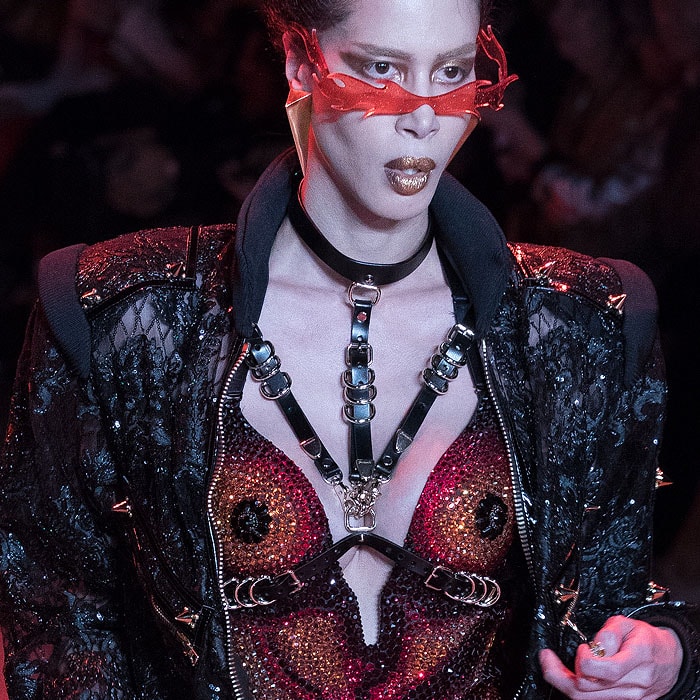 Model wearing flame sunglasses, a black leather harness, a multicolor-crystal bodysuit, and a spiked black zip jumpsuit at The Blonds Fall 2018 fashion show.