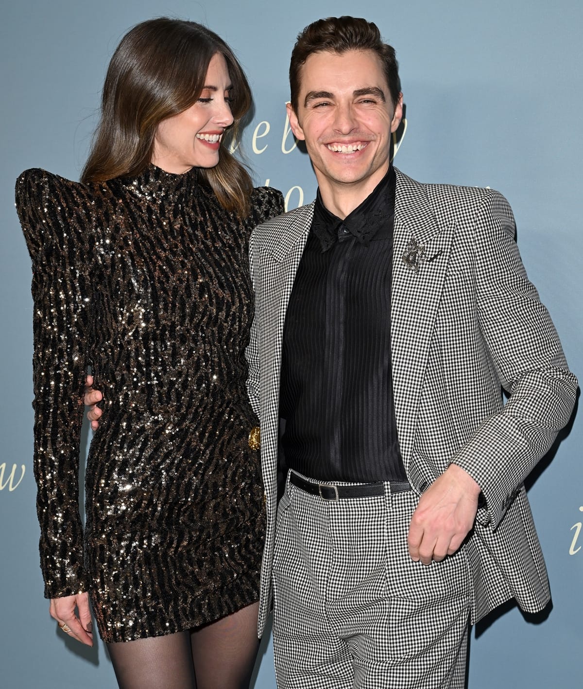 Alison Brie stuns in a black and gold sequin Balmain minidress with bold pagoda shoulders, while Dave Franco complements her look with a stylish micro-checked suit at the premiere of Somebody I Used to Know