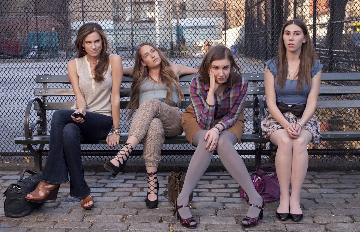 The main cast of Girls—Allison Williams, Jemima Kirke, Lena Dunham, and Zosia Mamet—relaxing on a bench in a scene from the show