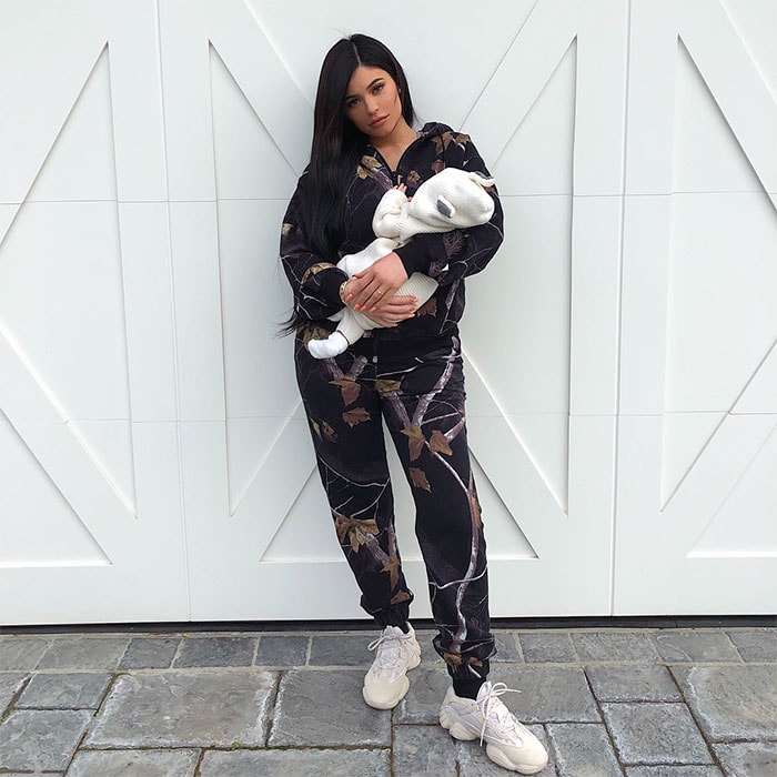 Kylie Jenner in Yeezy 'Desert Rat 500' sneakers holding her one-month old baby Stormi.