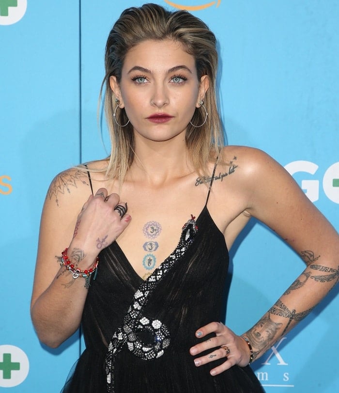 Paris Jackson proudly showcases her unique collection of tattoos, including intricate designs on her arms, hand, and chest, which add an edgy contrast to her elegant black Valentino gown adorned with a sparkling snake motif