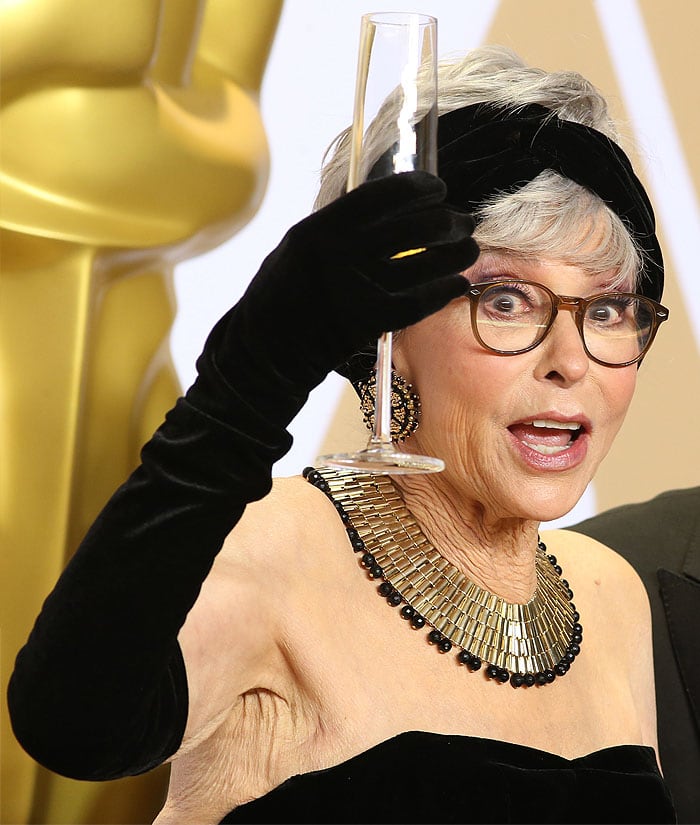 Rita Moreno holding champagne in the press room at the 2018 Academy Awards.