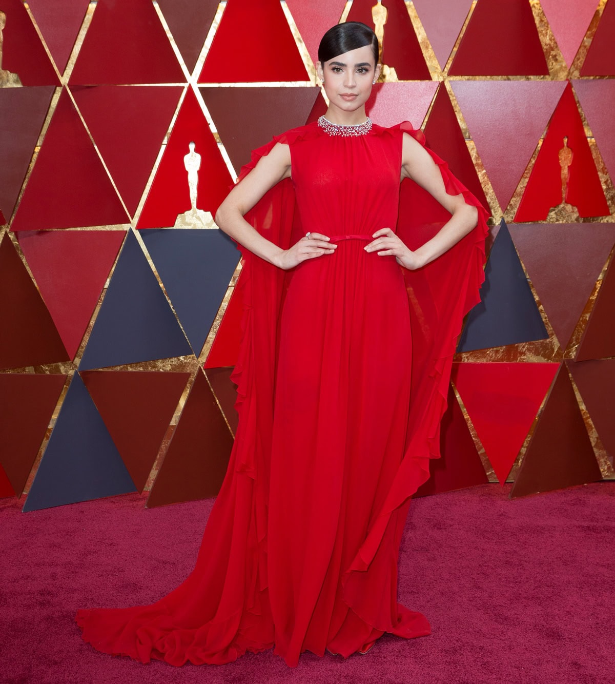Sofia Carson stuns in a flowing red Giambattista Valli gown, accented with Chopard diamonds and hidden Jimmy Choo pumps, as she arrives at the 2018 Oscars