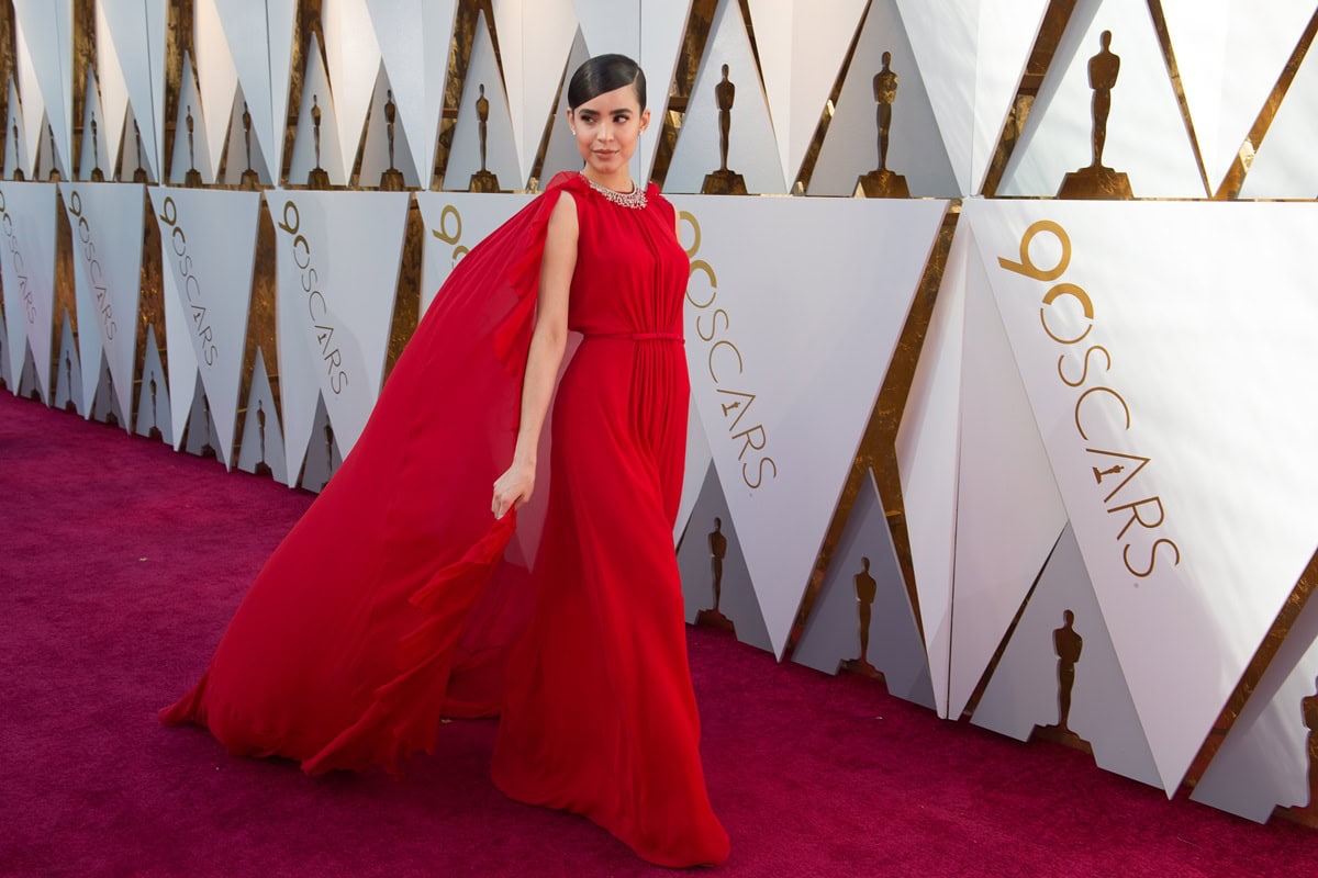 Sofia Carson sweeps across the 2018 Oscars red carpet in a billowing red Giambattista Valli gown, with her matching Jimmy Choo Anouk pumps just catching the light beneath the hem
