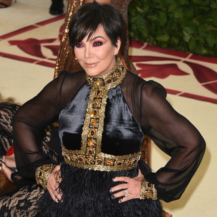 Kris Jenner in a black long-sleeve gown featuring gold and burgundy jeweled embellishments and a feather-embellished skirt