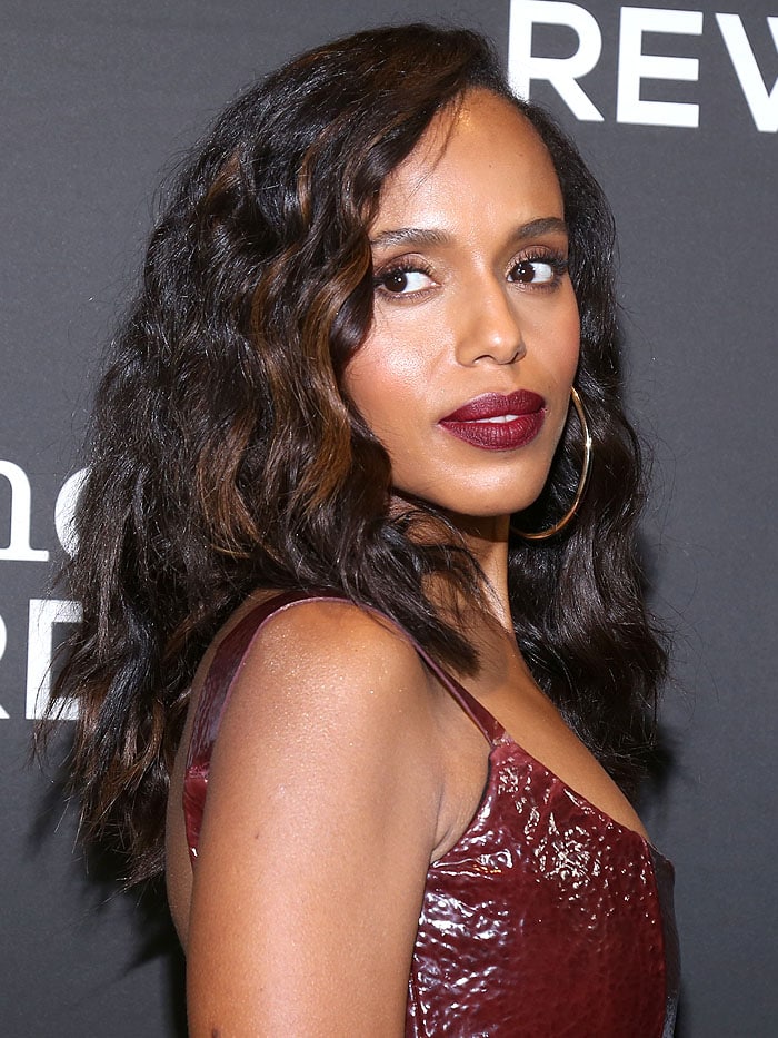 Kerry Washington wearing a Markarian Fall 2018 leather dress, gold hoop earrings, wine-red lipstick, and chunky brown highlights in her wavy hair.