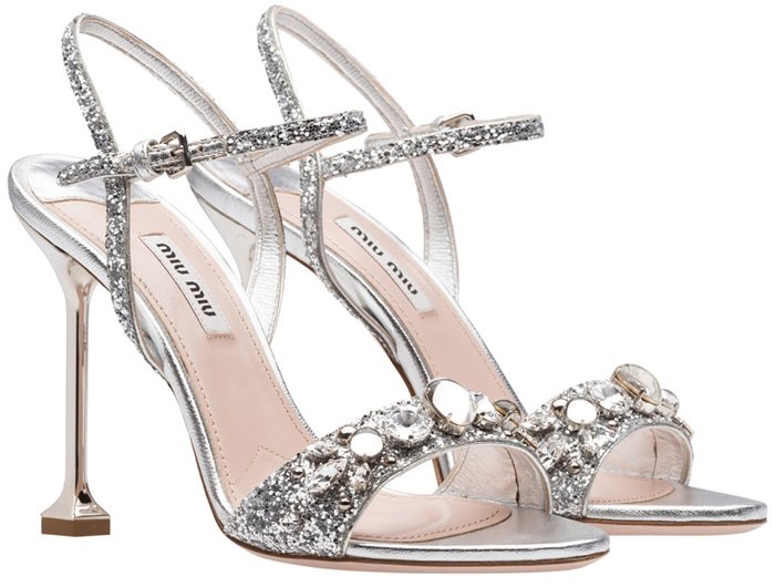 Crafted in Italy from metallic silver calf leather, these glittered sandals from Miu Miu feature a high stiletto heel, an ankle strap with a side buckle fastening, a branded insole, an open toe and Swarovski crystal embellishments